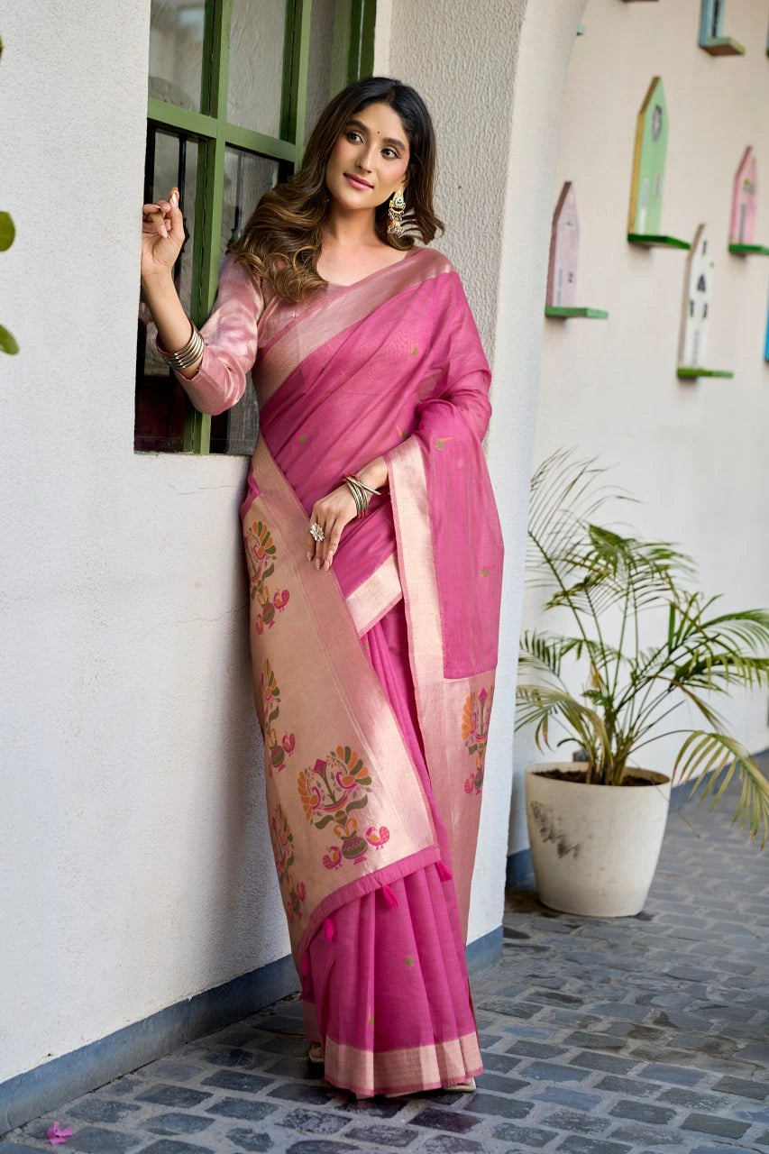 Woman in a pink saree standing against a white wall with decorative elements.